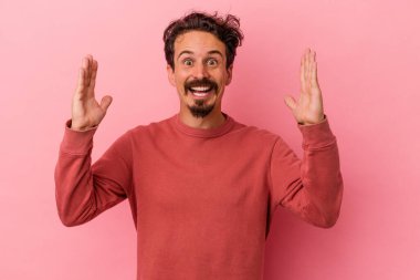 Pembe arka planda izole edilmiş genç beyaz adam hoş bir sürpriz alıyor, heyecanlı ve el kaldırıyor..