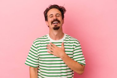Pembe arka planda izole edilmiş genç beyaz adam yüksek sesle gülüyor elini göğsünde tutuyor..