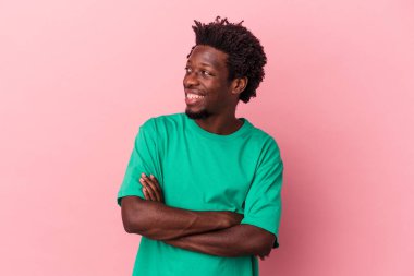 Pembe arka planda izole edilmiş genç Afro-Amerikalı adam kollarını kavuşturarak gülümsüyor..
