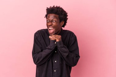 Pembe arka planda izole edilmiş genç Afrikalı Amerikalı ellerini çenesinin altında tutuyor ve mutlu bir şekilde yan tarafa bakıyor..