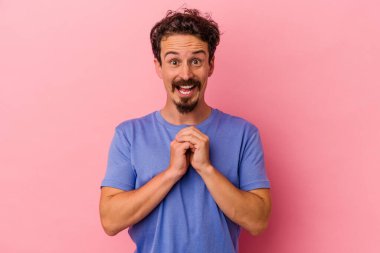Pembe arka planda izole edilmiş genç beyaz adam şans için dua ediyor, hayrete düşüyor ve ağzını açıp önüne bakıyor..