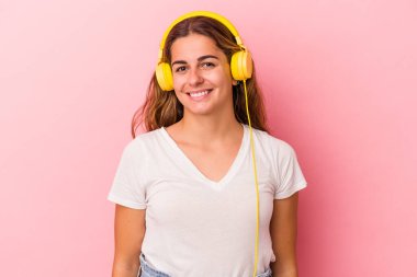 Pembe arka planda izole edilmiş müzik dinleyen genç beyaz kadın mutlu, güler yüzlü ve neşeli..