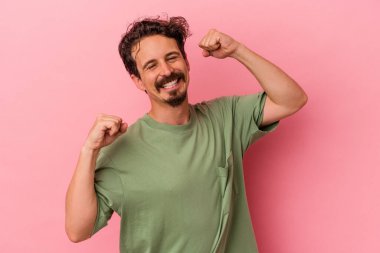 Pembe arka planda soyutlanmış genç beyaz adam özel bir günü kutluyor, atlıyor ve enerjiyle kollarını kaldırıyor..