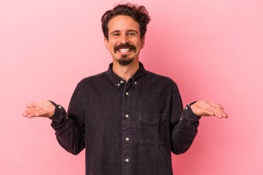 Pembe arka planda izole edilmiş genç beyaz adam kollarıyla ölçek oluşturuyor, mutlu ve kendinden emin hissediyor..