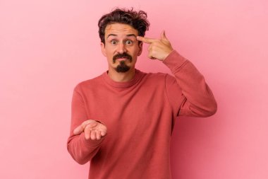 Pembe arka planda izole edilmiş genç beyaz adam elinde bir ürün tutuyor..