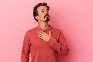 Pembe arka planda izole edilmiş genç beyaz adam yemin ediyor, elini göğsüne koyuyor..
