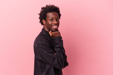 Genç Afrikalı Amerikalı adam pembe arka planda izole edilmiş mutlu ve kendinden emin gülümsüyor, elleriyle çenesine dokunuyor..