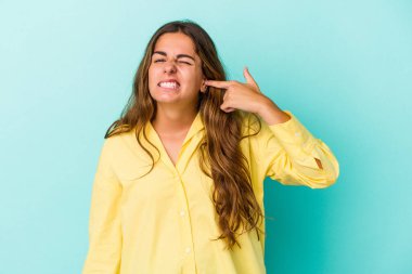 Genç beyaz kadın mavi arka planda izole edilmiş parmaklarıyla kulaklarını kapatıyor, gürültülü bir ortam yüzünden stresli ve çaresiz..