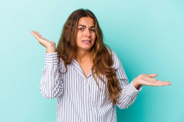 Kafkasyalı genç bir kadın mavi arka planda izole edilmiş. Kafası karışmış ve omuz silkiyor. Kopya alanını tutmak için..