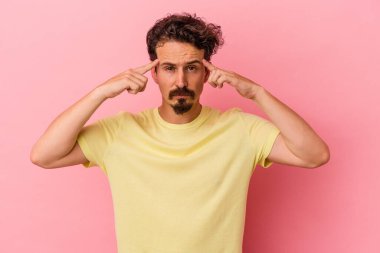 Pembe arka planda izole edilmiş genç beyaz adam bir göreve odaklanmış, parmaklarını işaret ediyor..