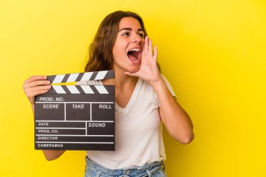 Sarı arka planda elinde klaket tutan genç beyaz kadın bağırıyor ve avuç içini açık tutuyordu..