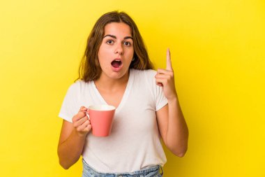 Kafkasyalı genç bir kadın sarı arka planda izole edilmiş bir kupa tutuyor. Bir fikri var, ilham verici bir kavram..