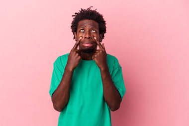 Genç Afrikalı Amerikalı bir adam pembe arka planda izole edilmiş ağlıyordu, bir şeyden mutsuzdu, acı ve kafa karışıklığı konsepti vardı..