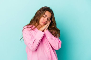 Mavi arka planda izole edilmiş genç beyaz kadın esniyor. Ağzı eliyle kapatan yorgun bir hareket sergiliyor..