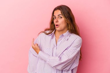 Pembe arka planda izole edilmiş genç beyaz kadın gülümsüyor ve boş alanda bir şeyler gösteriyor..