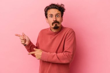 Pembe arka planda izole edilmiş genç beyaz adam işaret parmağıyla fotokopi alanını işaret ederek şok oldu..