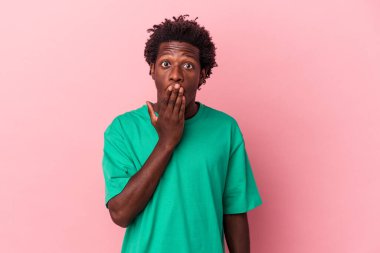 Genç Afrikalı Amerikalı bir adam pembe arka planda izole edilmiş. Şok olmuş, ağzı ellerle kaplanmış, yeni bir şey keşfetmeye hevesli..