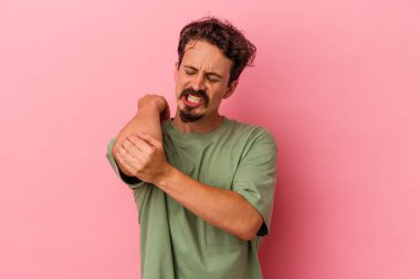 Genç beyaz adam pembe arka planda izole edilmiş dirsek masajı yapıyor, kötü bir hareketin ardından acı çekiyor..