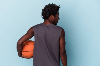 Basketbol oynayan genç Afrikalı Amerikalı adam mavi arka planda izole edilmiş.
