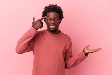 Genç Afrikalı Amerikalı bir adam pembe arka planda izole edilmiş ve elinde bir ürün tutuyor..