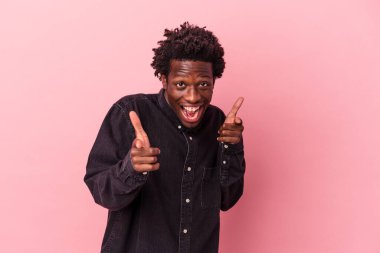 Genç Afro-Amerikalı adam pembe arka planda izole edilmiş neşeli gülümsemeler ön tarafı işaret ediyor..