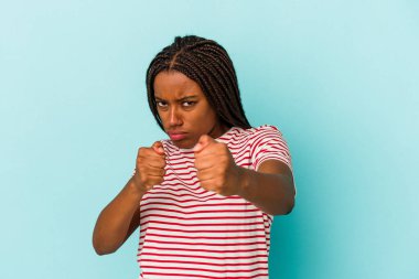 Genç Afro-Amerikalı bir kadın mavi arka planda izole edilmiş. Bir tartışma yüzünden yumruk atıyor, sinirleniyor, kavga ediyor..
