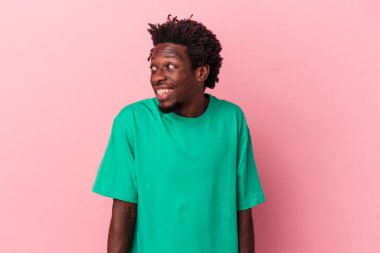 Genç Afrikalı Amerikalı bir adam pembe arka planda izole edilmiş, gülüyor ve gözlerini kapatıyor, rahatlamış ve mutlu hissediyor..