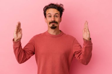 Pembe arka planda izole edilmiş genç beyaz adam işaret parmaklarıyla küçük bir şey tutuyor, gülümsüyor ve kendinden emin..