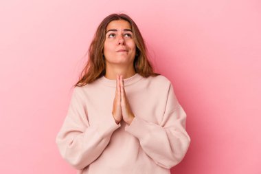 Pembe arka planda soyutlanmış genç beyaz bir kadın el ele tutuşup ağzının kenarında dua ediyor, kendinden emin hissediyor..