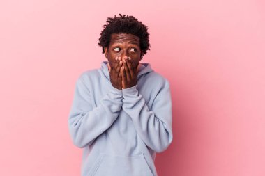 Genç Afrikalı Amerikalı bir adam pembe arka planda izole edilmiş düşünceli bir şekilde bir fotokopi odasına bakıyor elleriyle ağzını kapatıyor..