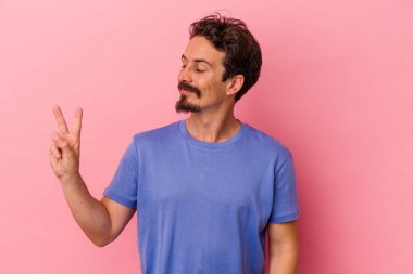 Genç beyaz adam pembe arka planda izole edilmiş neşeli ve kaygısız parmakları olan bir barış sembolü gösteriyor..