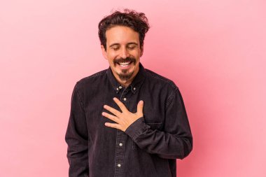 Pembe arka planda izole edilmiş genç beyaz adam yüksek sesle gülüyor elini göğsünde tutuyor..