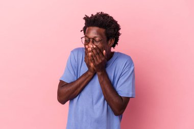 Genç Afrikalı Amerikalı bir adam pembe arka planda izole edilmiş bir şekilde bir şeylere gülüyor, elleriyle ağzını kapatıyor..
