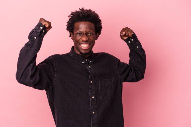 Genç Afrikalı Amerikalı adam pembe arka planda izole edilmiş tasasız ve heyecanlı bir şekilde tezahürat yapıyor. Zafer konsepti.