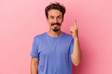 Pembe arka planda izole edilmiş genç beyaz adam iki parmağı da boş bir alan gösteriyor..