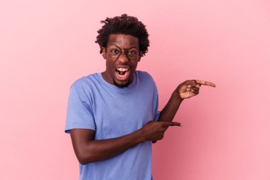 Genç Afrikalı Amerikalı bir adam pembe arka planda izole edilmiş, işaret parmaklarıyla fotokopi alanını işaret ederek heyecan ve arzusunu ifade ediyor..