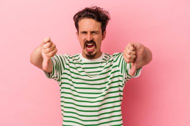 Pembe arka planda izole edilmiş genç beyaz adam baş parmağını aşağı gösteriyor ve hoşlanmadığını ifade ediyor..