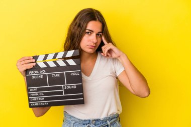 Elinde klaket tutan beyaz bir kadın sarı arka planda izole edilmiş. Şakağı işaret ediyor. Düşünüyor, bir göreve odaklanıyor..