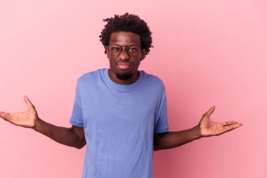 Genç Afrikalı Amerikalı, pembe arka planda izole edilmiş. Sorgulama sırasında omuz silkiyor ve şüphe ediyor..