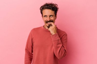 Pembe arka planda izole edilmiş genç beyaz adam rahatlamış bir şeyin fotokopi odasına baktığını düşünüyor..