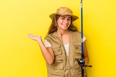 Sarı arka planda izole edilmiş bir çubuk tutan genç beyaz balıkçı bir avuç içinde fotokopi alanı ve belinde başka bir el tutan.