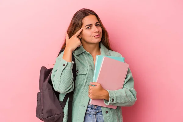 ピンクの背景にピンク色の寺院を指差した本を持っている若い白人学生の女性 タスクに焦点を当てました — ストック写真