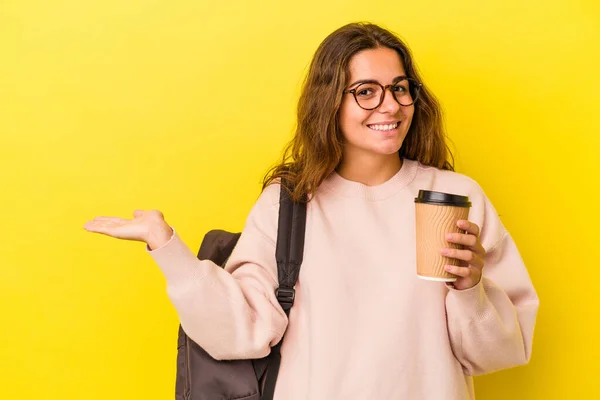 年轻的高加索女学生拿着用黄色背景隔开的咖啡 手掌上有一个复制的空间 腰部有另一只手 — 图库照片