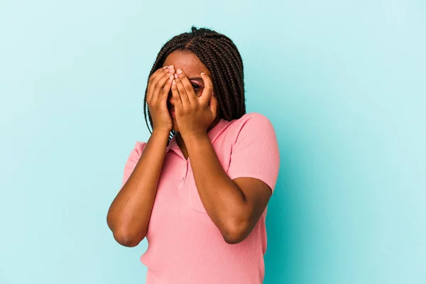 Młoda Afroamerykanka Odizolowana Niebieskim Tle Mruga Kamery Przez Palce Zakłopotana — Zdjęcie stockowe