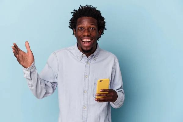 一个拿着蓝色背景的手机的年轻的非洲裔美国人得到了一个愉快的惊喜 兴奋地举起了手 — 图库照片