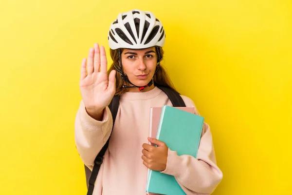 若いですCaucasian学生女性を身に着けています自転車ヘルメット黄色の背景に隔離されたスタンドとともにアウトストップサインを示す あなたを防ぎます — ストック写真