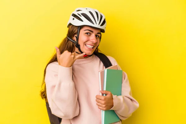 若いです白人学生女性身に着けています自転車ヘルメット黄色の背景に隔離された携帯電話の呼び出しジェスチャーとともに指 — ストック写真