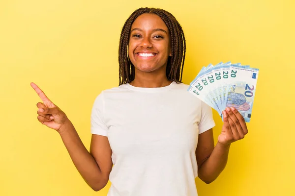 Mladá Afroameričanka Drží Bankovky Izolované Žlutém Pozadí Usmívá Ukazuje Stranou — Stock fotografie