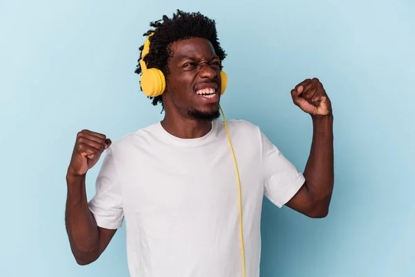 勝利の後に拳を上げ青の背景に隔離された音楽を聞いている若いアフリカ系アメリカ人の男性 勝者の概念 — ストック写真