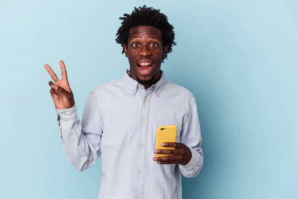 年轻的非洲裔美国人拿着手机 用蓝色背景隔离 快乐而无忧无虑 用手指展示和平的象征 — 图库照片